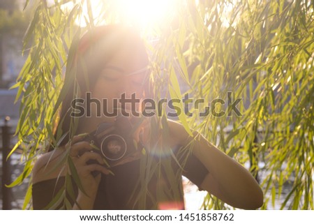 Backlit blurry low contrast Asian Girl with camera in the park in sunset time. Brunette girl with film camera in the vintage colored image