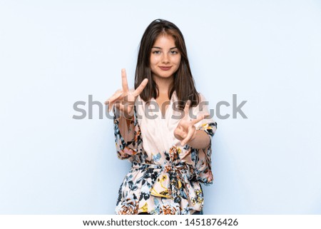 Caucasian girl with kimono over isolated blue background smiling and showing victory sign