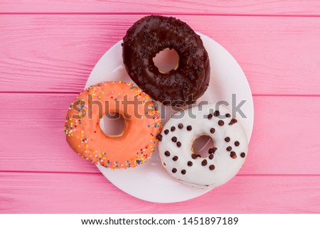 Three donuts on plate, top view. Different donuts on pink wooden background.