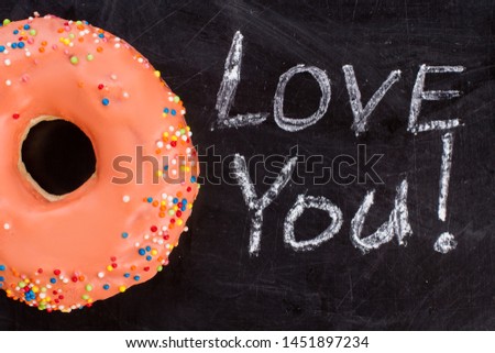 Orange donut and inscription I love you on chalk board. Iced donut with sprinkles on black background. Sweets for Valentines Day.
