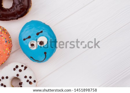 Sweets on wooden table. Blue donut with funny eyes on white wooden surface. Space for text.