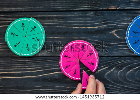 Kids hand moves colorful math fractions on dark wooden background or table. Interesting creative funny math for kids. Education, back to school concept. Geometry and mathematics materials.