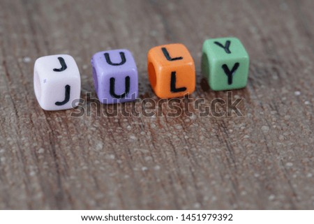 selective focus. July word made of colourful alphabet square beads on the wooden background