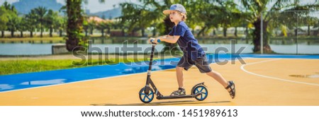 BANNER, LONG FORMAT Happy child on kick scooter in on the basketball court. Kids learn to skate roller board. Little boy skating on sunny summer day. Outdoor activity for children on safe residential