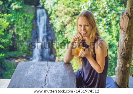 Closeup portrait image of a beautiful woman drinking ice tea with feeling happy in green nature and waterfall garden background