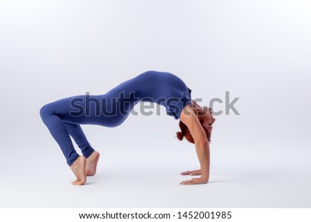 Beautiful slim woman in sports overalls  doing yoga, standing in an asana balancing pose - bridge outside of an overt bow on white  isolated background. The concept of sports and meditation. 