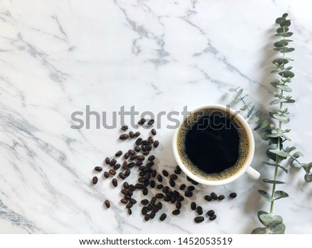 Top view white cup contained unsweetened coffee on marble table background with coffee beans and eucalyptus branches. (space for text, horizontal photography)