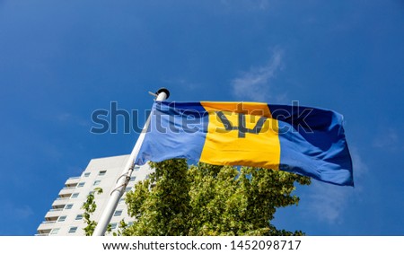 Barbados flag. National symbol waving on pole, Highrise building and clear blue sky background, sunny day. Indepedence day concept.