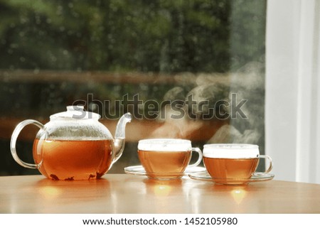 Teapot and cups of hot tea on wooden table against blurred background, space for text