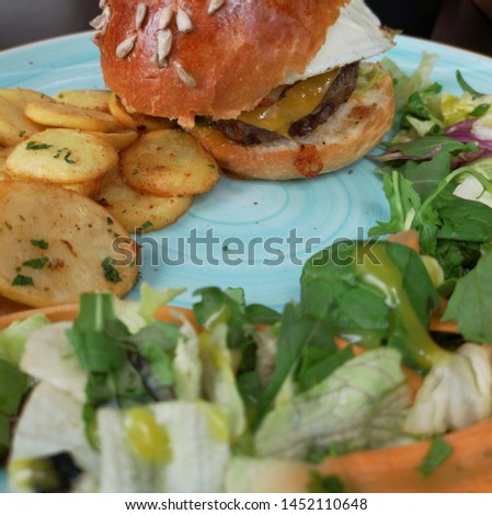 Close-up, side view of a hamburger bun, chips and green salad.