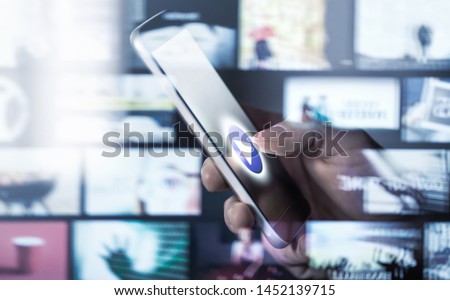Watching movies and series with smartphone. On demand (VOD) service. Future multimedia technology in mobile phone. Man pressing play button. Entertainment of tv network. Many online video thumbnails. Royalty-Free Stock Photo #1452139715