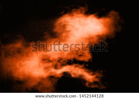Freeze motion of orange powder exploding  on black background. Abstract design of color dust cloud. Particles explosion.