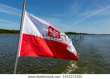 Polish flag suspended on the stern of a small inland ship. A vessel floating on a large lake in central Europe. Season of the summer.