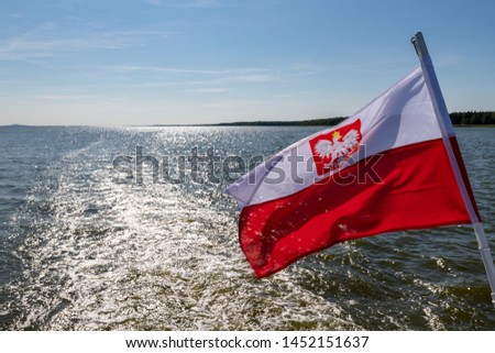 Polish flag suspended on the stern of a small inland ship. A vessel floating on a large lake in central Europe. Season of the summer.