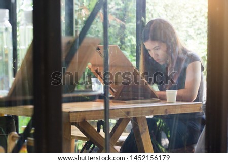 Beautiful woman embodying her ideas on paper with help of paintbrush and watercolors, interior of coffee cafe on natural background.