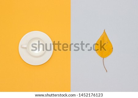 White empty cup with saucer and autumn leaf on yellow and gray background. Copy space Flat lay Mock up Template for your design.
