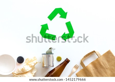 Green recycling sign with waste materials, bottles, cups, paper bag on white background top view
