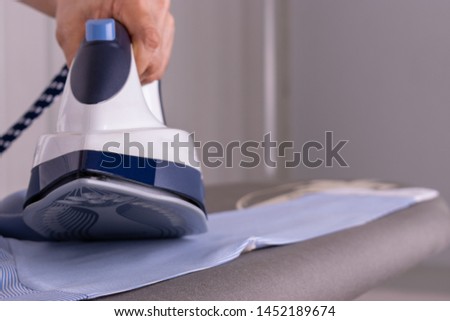 Close-up woman ironing clothes on ironing board in laundry room at home.