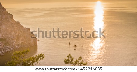 people on the paddle boards floating on the lake at sunset. Paddle surfing on lake Baikal. Russia, Siberia, Baikal.