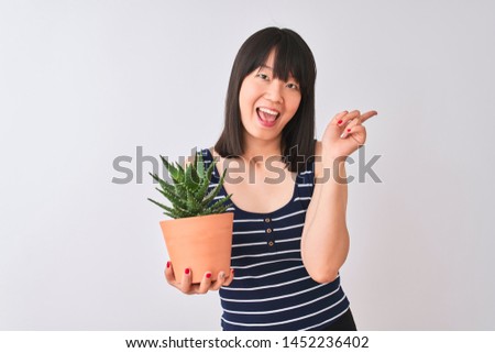 Young beautiful Chinese woman holding cactus pot over isolated white background very happy pointing with hand and finger to the side