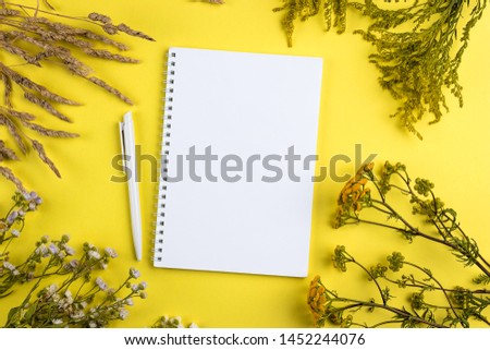 Creative summer layout made of wildflowers and dry grass on yellow background. Minimal summer exotic concept with copy space. White notebook arrangement background.