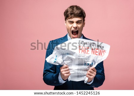 aggressive businessman crumpling newspaper with fake news while looking at camera 