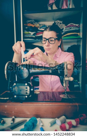 Young woman seamstress using retro sewing machine at home. Vintage edited photo.