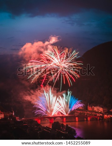 Fireworks celebrating the Heidelberger Schlossbeleuchtung in Heidelberg, Germany. Photo includes the Neckar river and the Heidelberg Old Bridge and twilight off in the distance. 