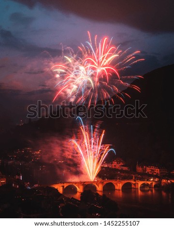 Fireworks celebrating the Heidelberger Schlossbeleuchtung in Heidelberg, Germany. Photo includes the Neckar river and the Heidelberg Old Bridge and twilight off in the distance. 