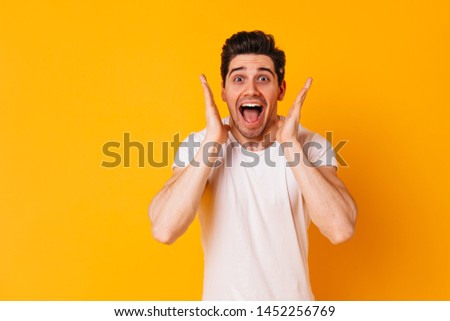 Funny man in white outfit shouts joyfully and looks enthusiastically at camera on orange background