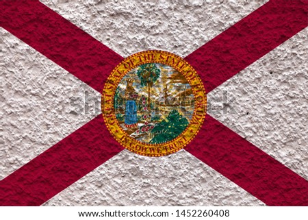 The national flag of the US state Florida in against a gray wall with stony surface on the day of independence in colors of red and white. Political and religious disputes, customs and delivery.