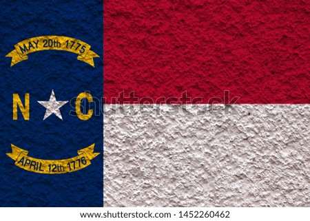 The national flag of the US state North Carolina in against a gray wall stony surface on the day of independence in blue red and white. Political and religious disputes, customs and delivery.