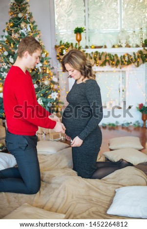Beautiful pregnant couple in love on the background of a Christmas tree, having a rest on Christmas holidays before the new year. Big pregnant belly
