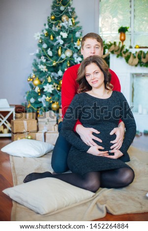 Beautiful pregnant couple in love on the background of a Christmas tree, having a rest on Christmas holidays before the new year. Big pregnant belly
