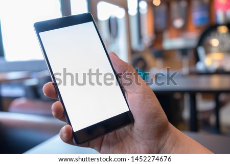 Man's hands holding mobile phone at cofee shop with blank white screen can be add your texts or others, empty copy space for advertising, product display. Royalty-Free Stock Photo #1452274676