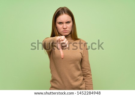 Young woman with turtleneck sweater showing thumb down with negative expression