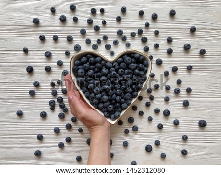 Hand holding plate of  blueberries on wood background. Heart shaped. Food Photography.