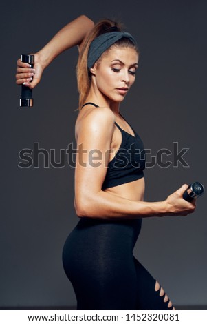 A woman with a slender figure involved in sports with dumbbells in the hands of leggings  