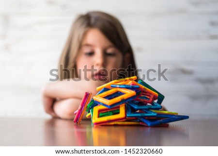 Portrait of beautiful thoughtful little girl playing colorful magnet plastic blocks kit, daydreaming and creating picture ideas in her mind. Creative process. Education and school concept