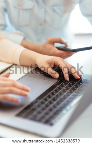 Girls dressed in casual discuss work issues, hands on a laptop