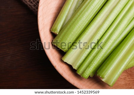 Fresh ripe green crisp sliced celery in deep wooden bowl on dark wooden background.