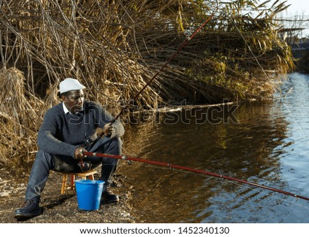 Portrait of bored African man fishing with rods on river