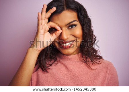 Young beautiful transsexual transgender woman standing over isolated pink background with happy face smiling doing ok sign with hand on eye looking through fingers