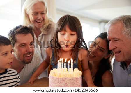 Six year old white girl celebrating her birthday with family blowing out the candles on her cake Royalty-Free Stock Photo #1452345566