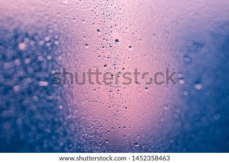Drops on the window. Panoramic rainy view. Wet glass surface. Abstract pink and blue background with beautiful bokeh. Moody wallpaper