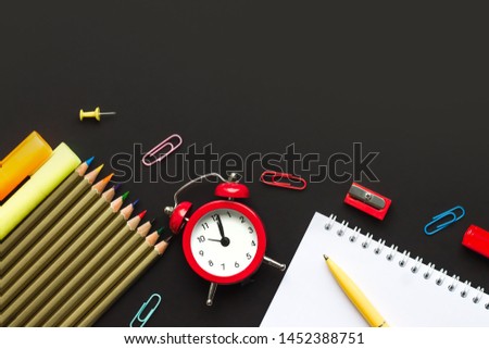 School supplies on a black background with copy space for text. Pencils, scissors, red alarm clock, notebook top view. Back to school