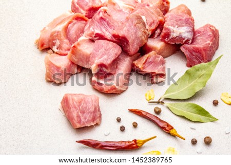 Raw fresh pork shoulder, cut into pieces with spices. Cooking healthy protein food concept. Dried bay leaves, chilli and black pepper, allspice, garlic pieces. Concrete background, close up