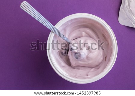 Yogurt cup with blue berry yoghurt, spoon and foil lid isolated on purple background - top view photograph Royalty-Free Stock Photo #1452397985