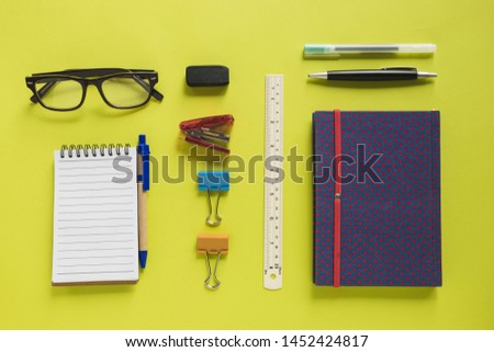 Overhead view of various stationeries on yellow background
