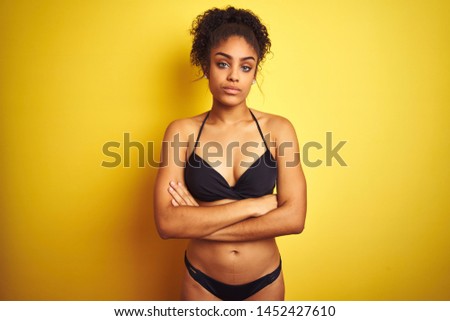 African american woman on vacation wearing bikini standing over isolated yellow background skeptic and nervous, disapproving expression on face with crossed arms. Negative person.